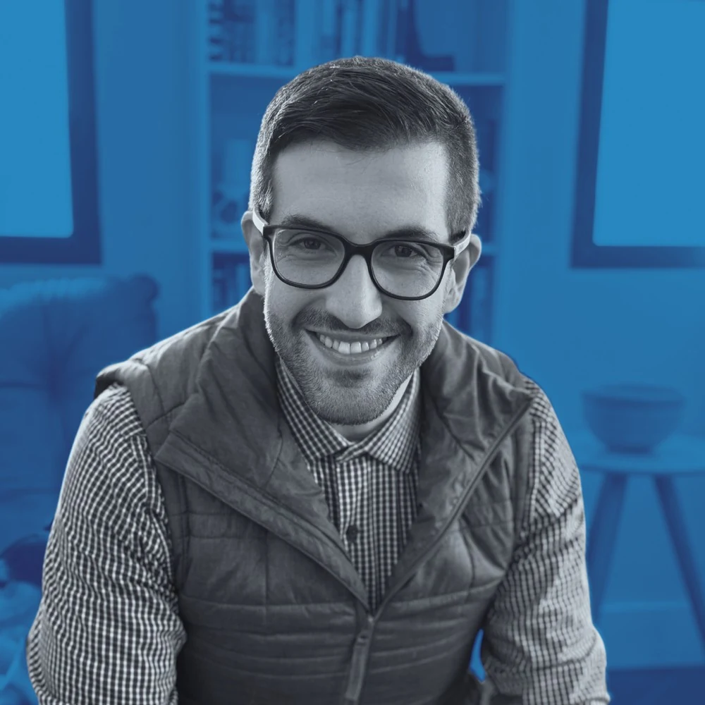 Retrato de Cauê Madeira sorrindo, de óculos e colete, em tons de azul